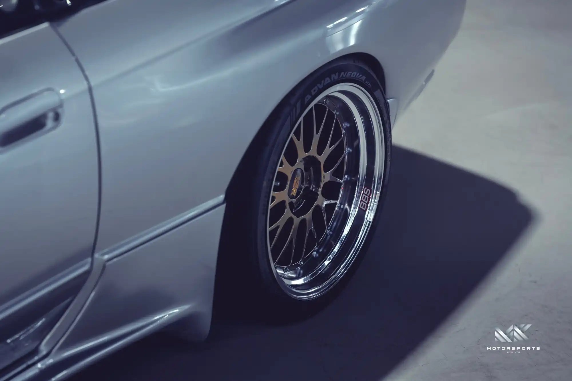 A silver car with multi-spoke chrome wheels.