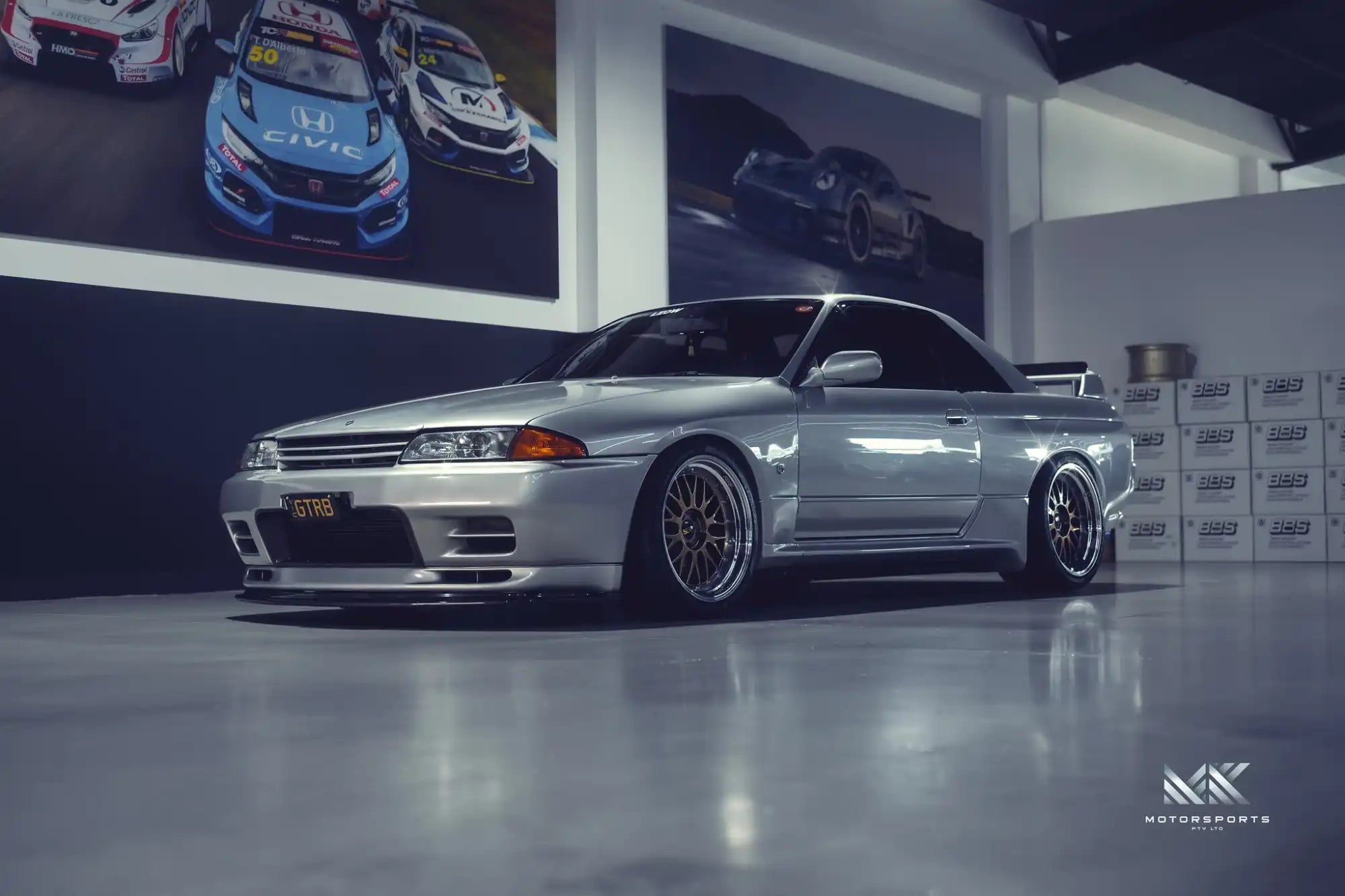 A silver Nissan Skyline R32 GT-R coupe with aftermarket wheels.