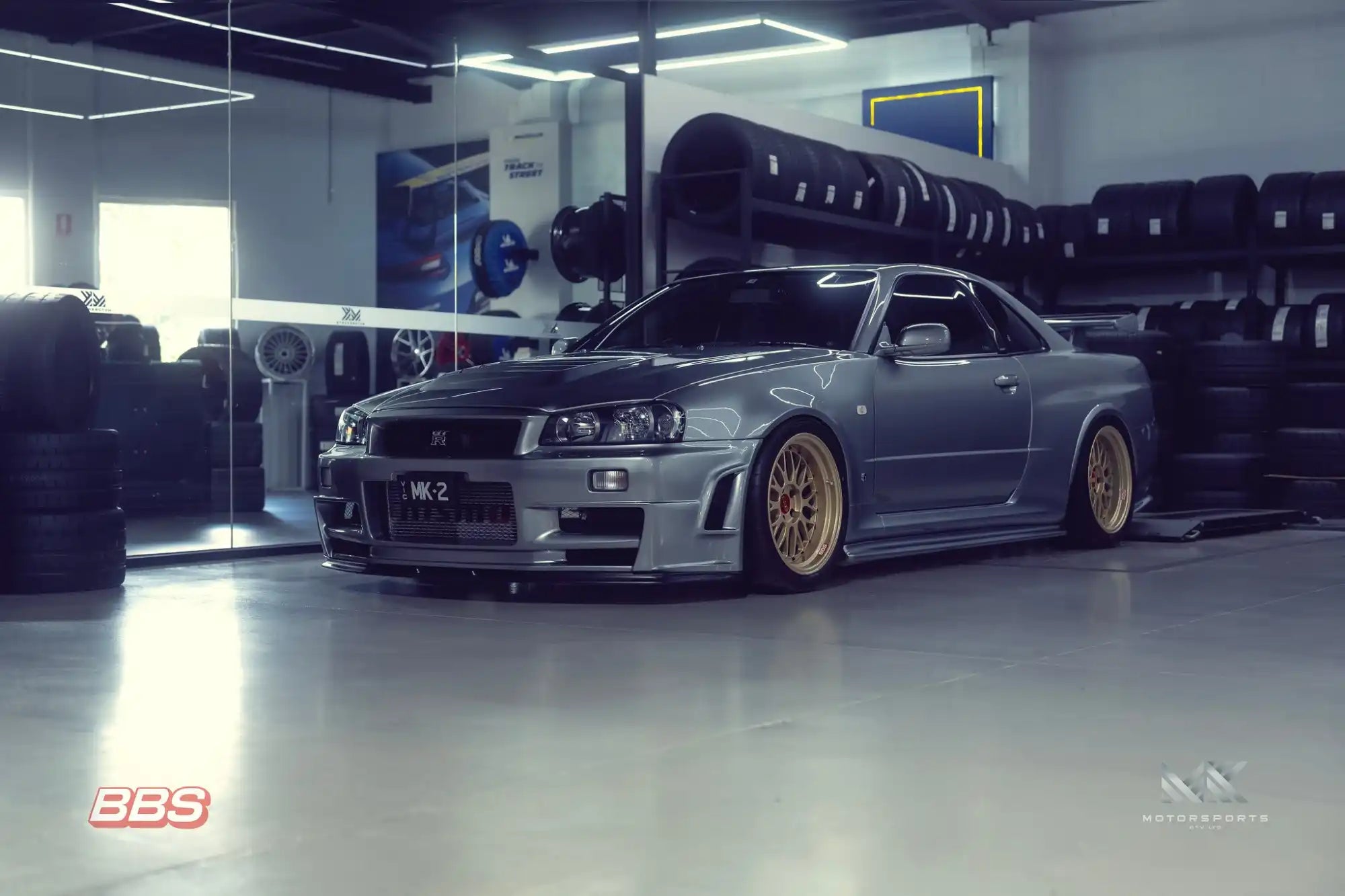 A silver Nissan Skyline R34 GT-R with gold BBS wheels.