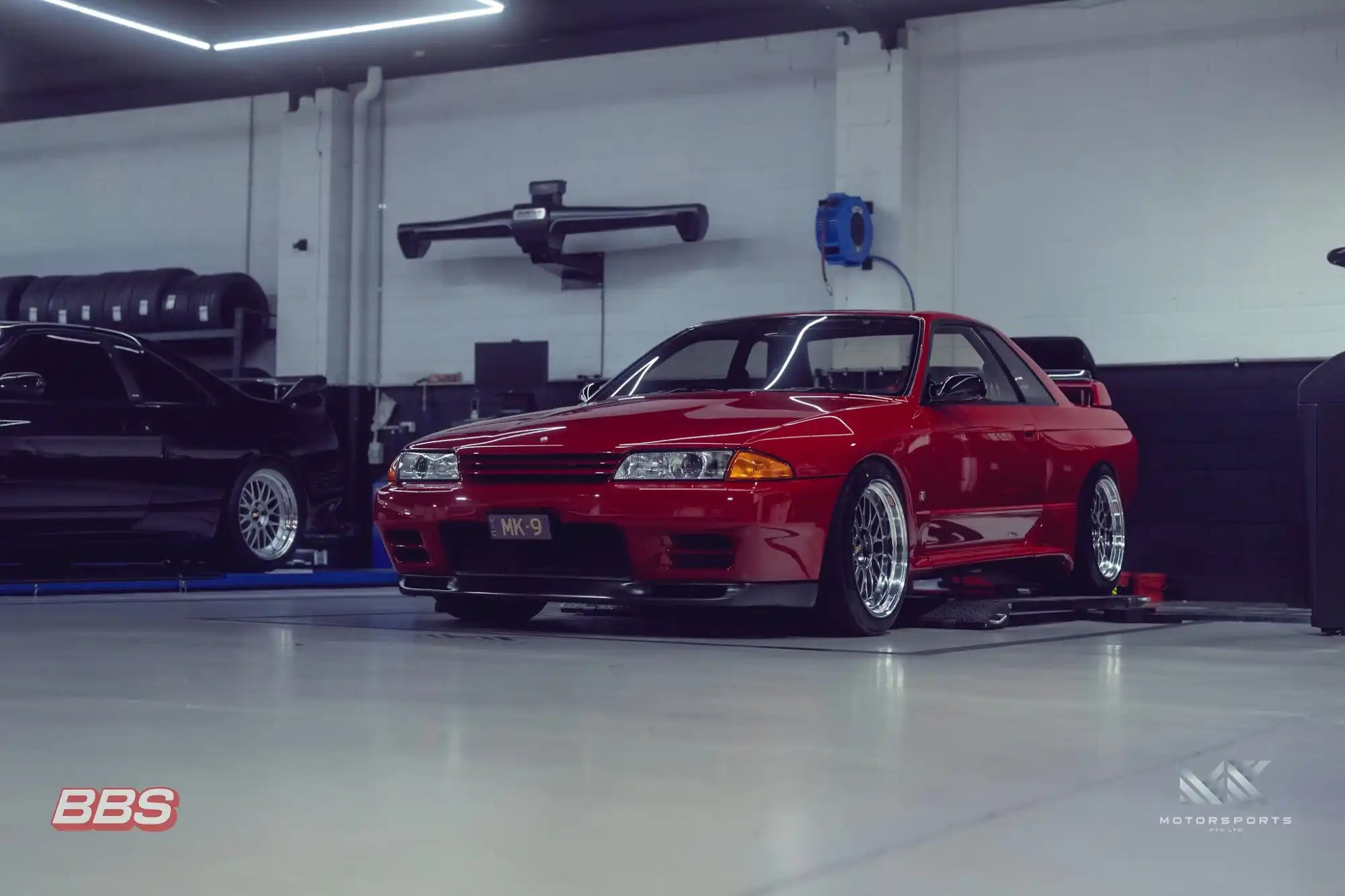 A vibrant red Nissan Skyline R32 GT-R coupe with aftermarket wheels.