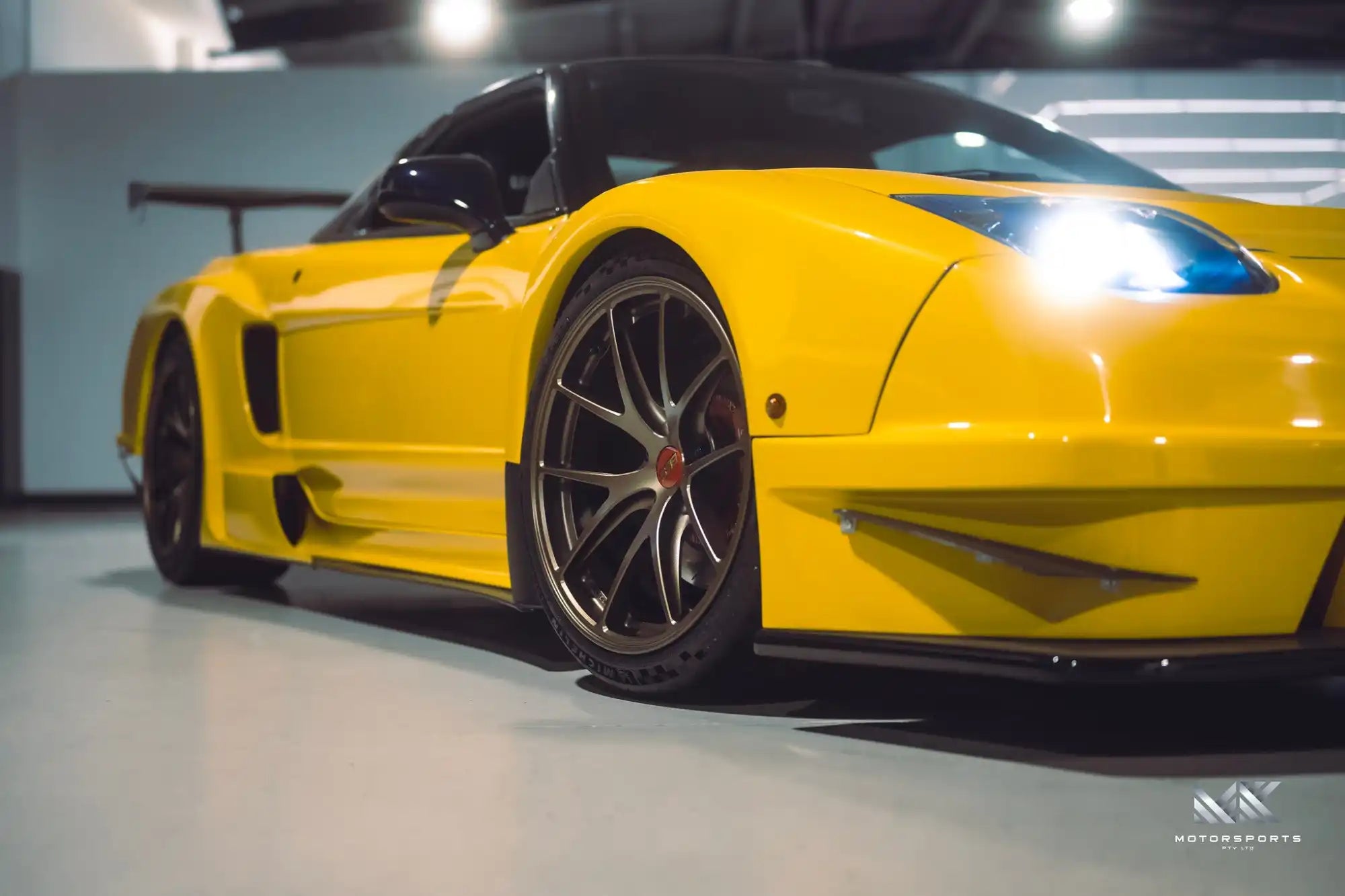 Bright yellow sports car with custom wheels and a large rear spoiler.