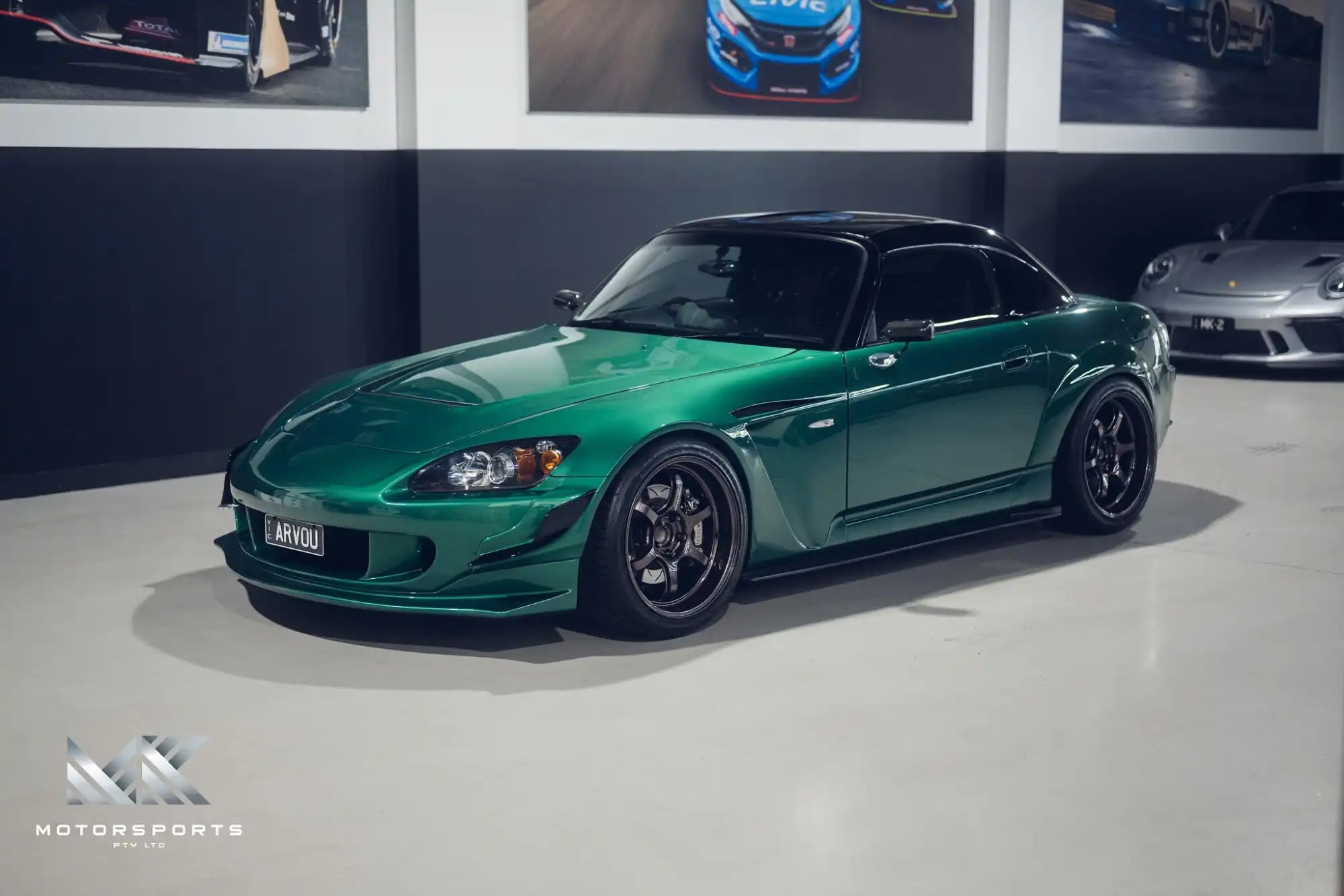 A custom metallic green Honda S2000 with a black hardtop and aftermarket black wheels.