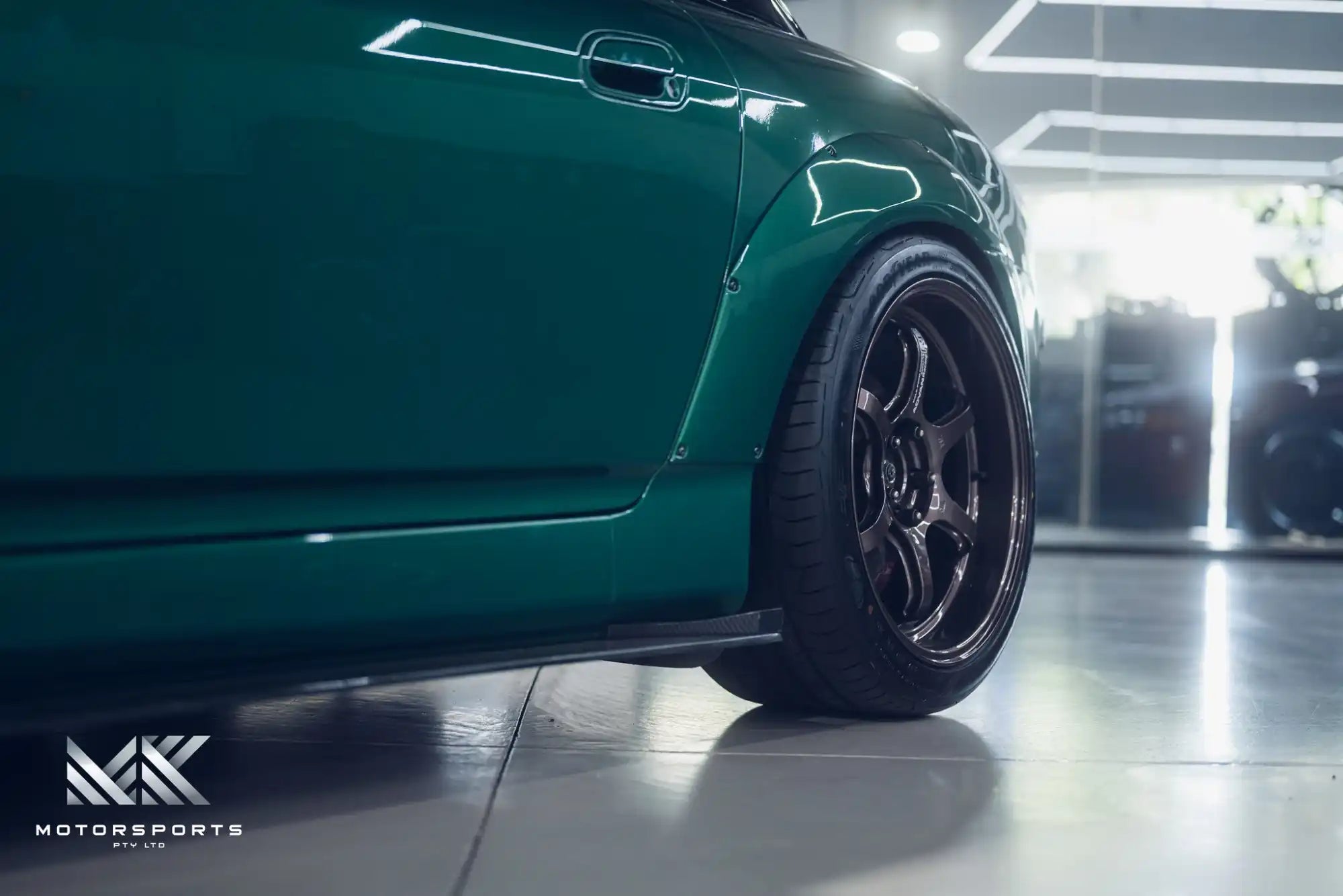 A custom-modified green sports car with wide fender flares and black multi-spoke wheels.