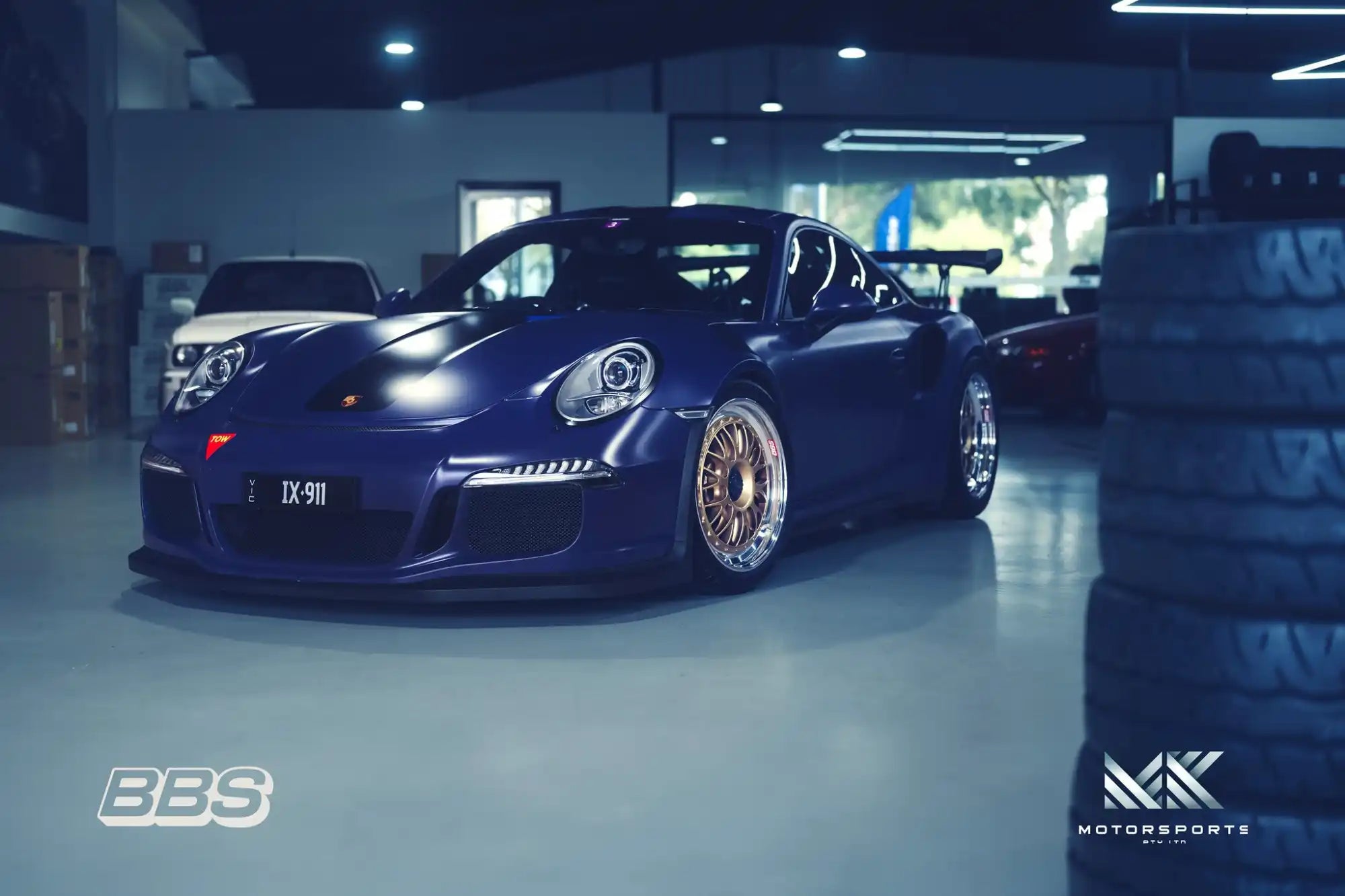 A dark blue Porsche 911 sports car with gold multi-spoke wheels.