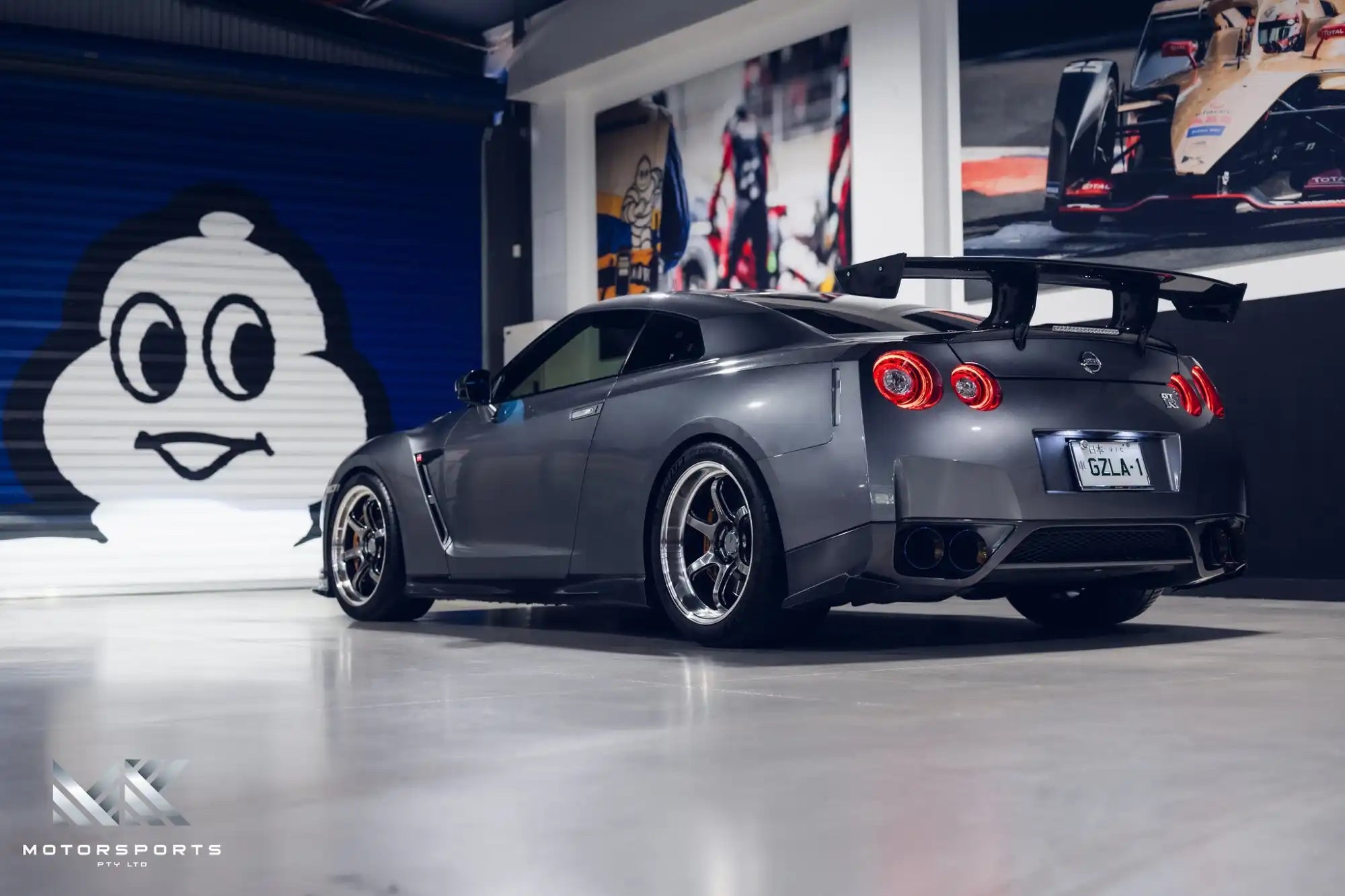 A dark gray Nissan GT-R sports car with a large rear wing and aftermarket wheels.