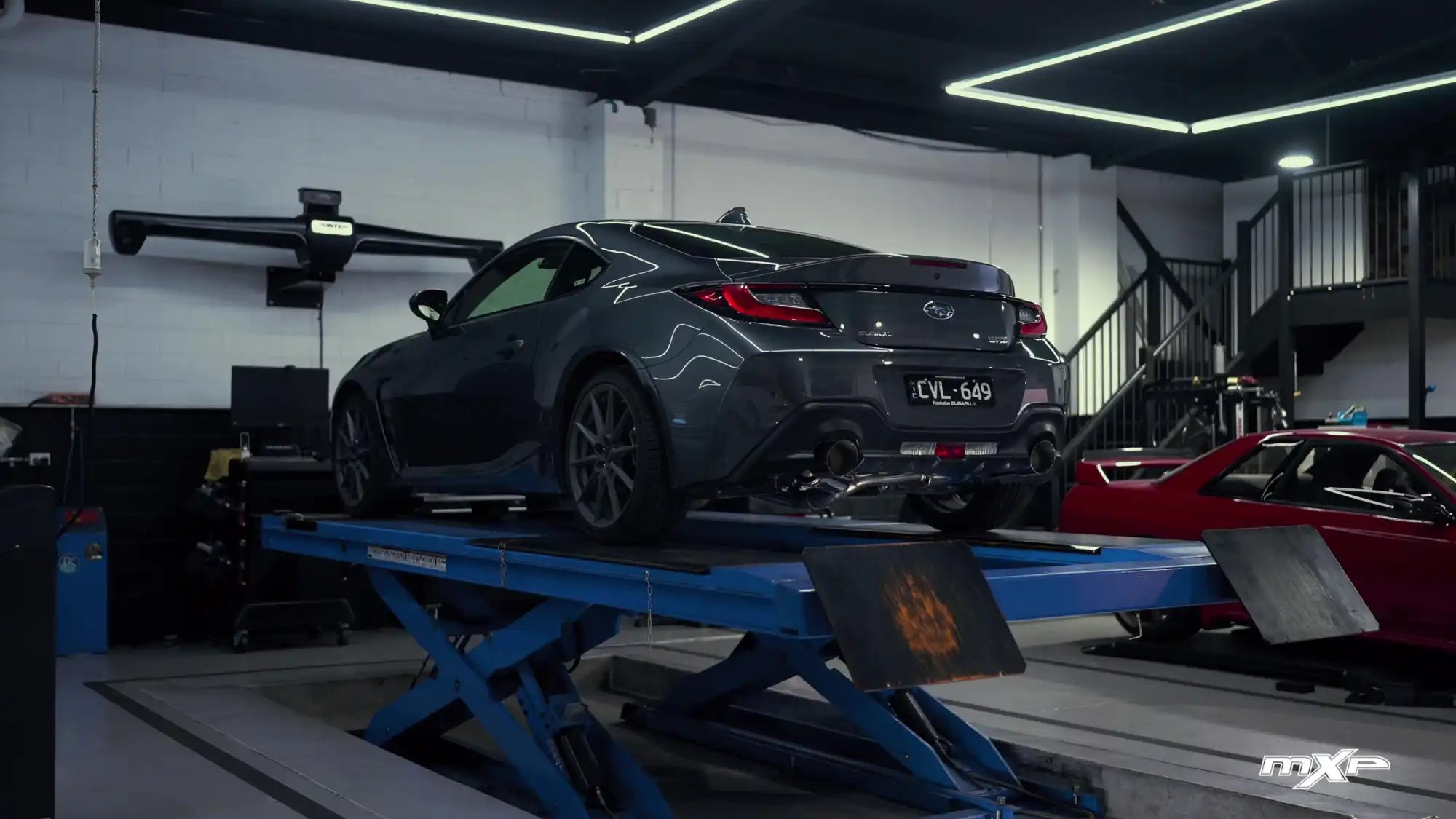 A dark grey sports coupe on a vehicle lift.