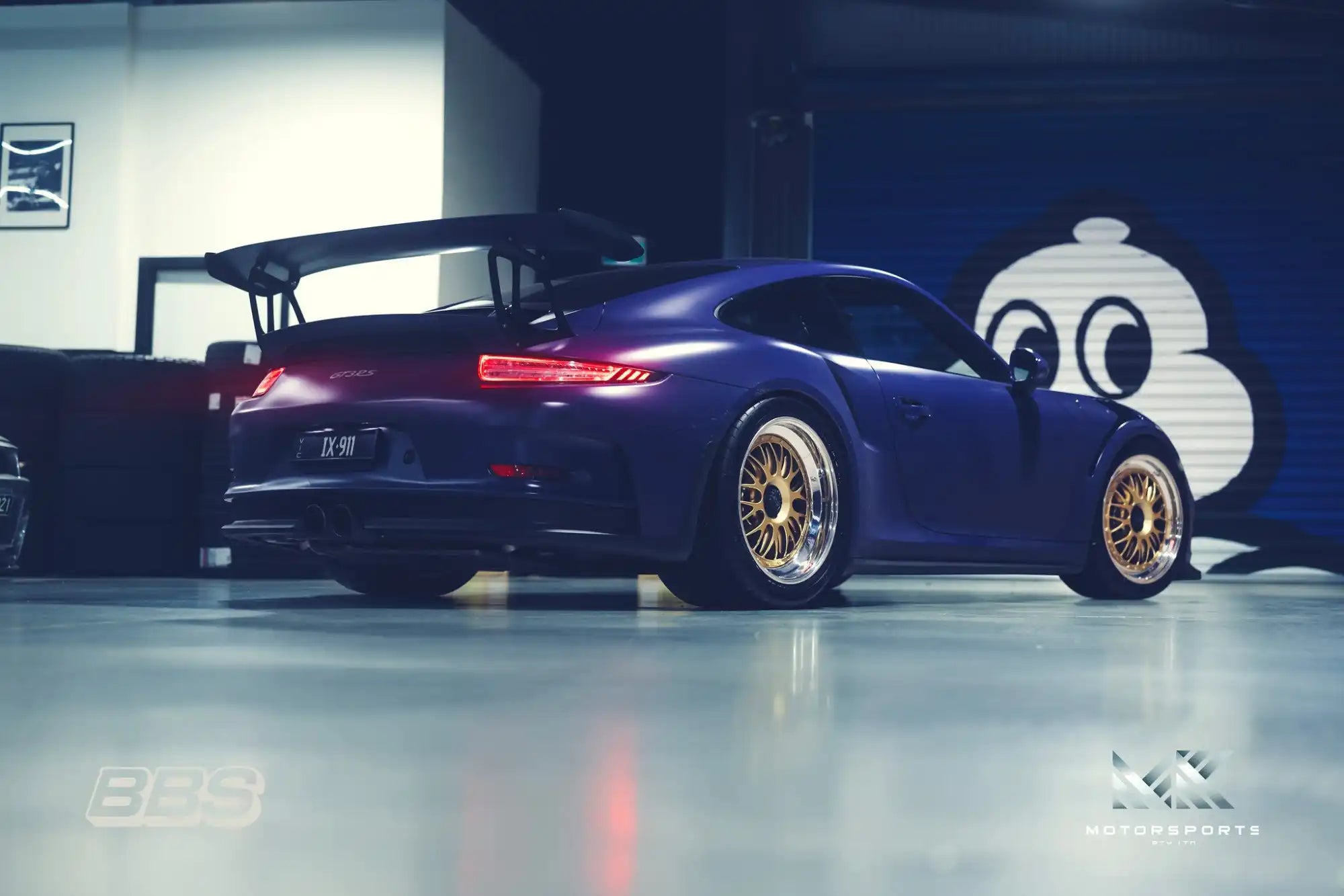 A dark purple Porsche with gold multi-spoke wheels and a large rear wing.