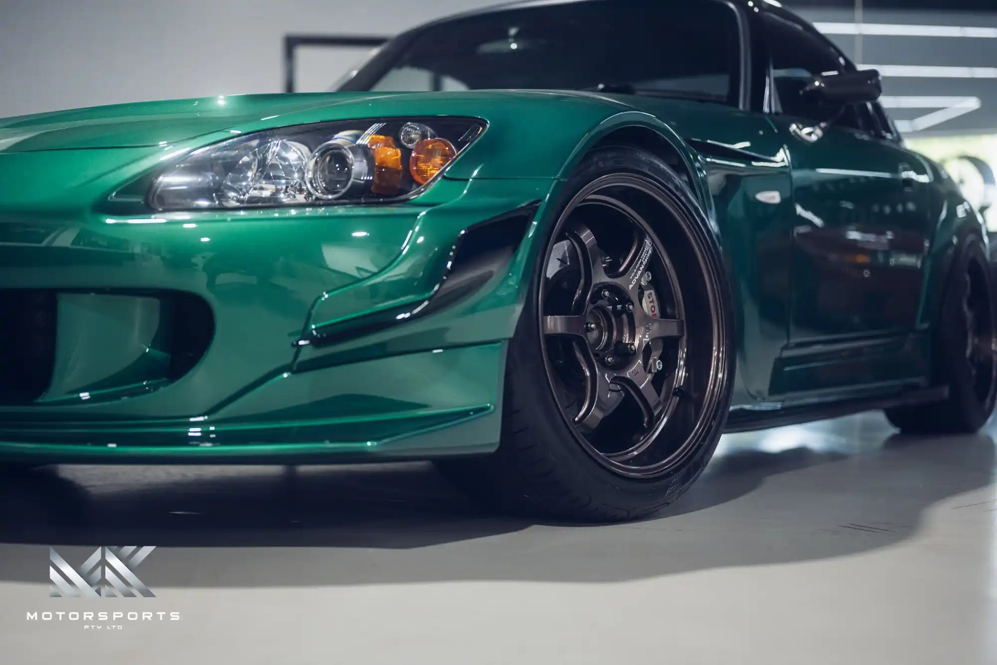 A green Honda S2000 sports car with custom wheels and body kit.