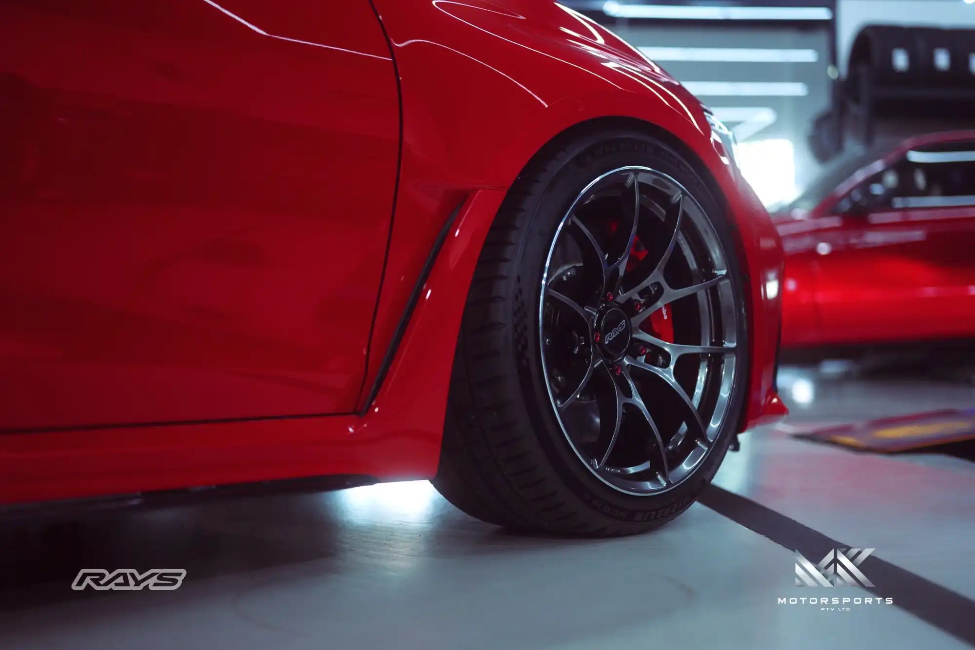 A shiny red sports car with custom dark grey alloy wheels.