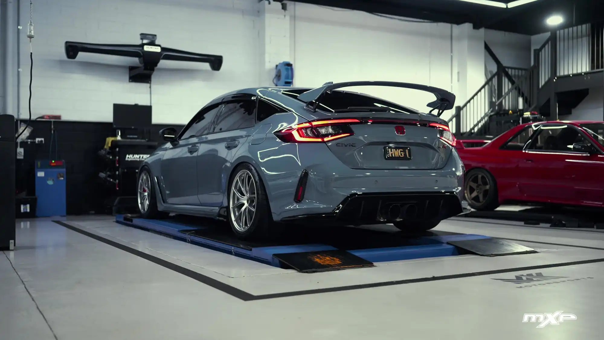 A sleek, gray Honda Civic Type R with a large rear spoiler and custom wheels, parked on a diagnostic lift.