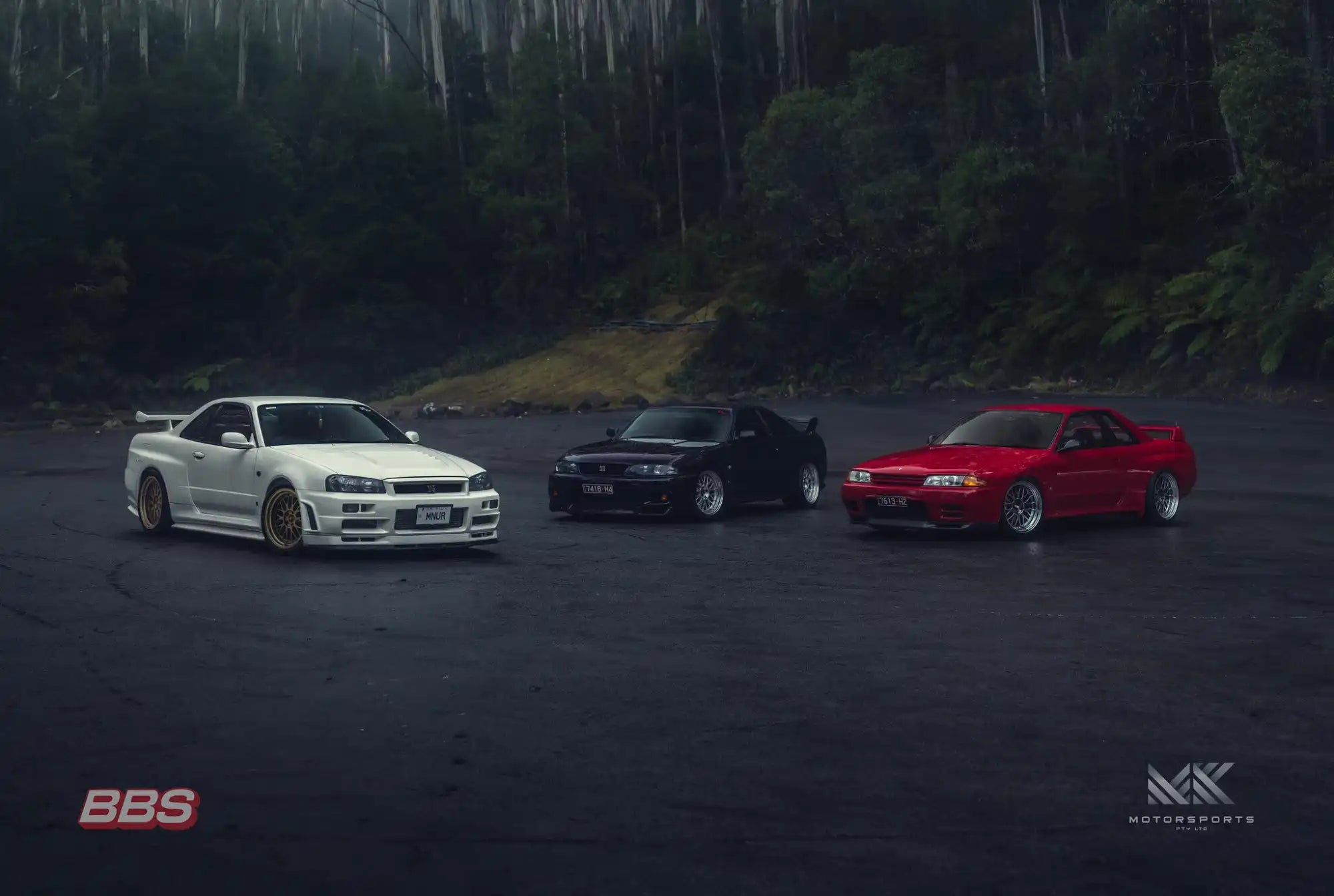 Three modified Japanese sports cars, including a white Nissan Skyline GT-R R34, a black Nissan Skyline GT-R R33, and a red Nissan Skyline GT-R R32.