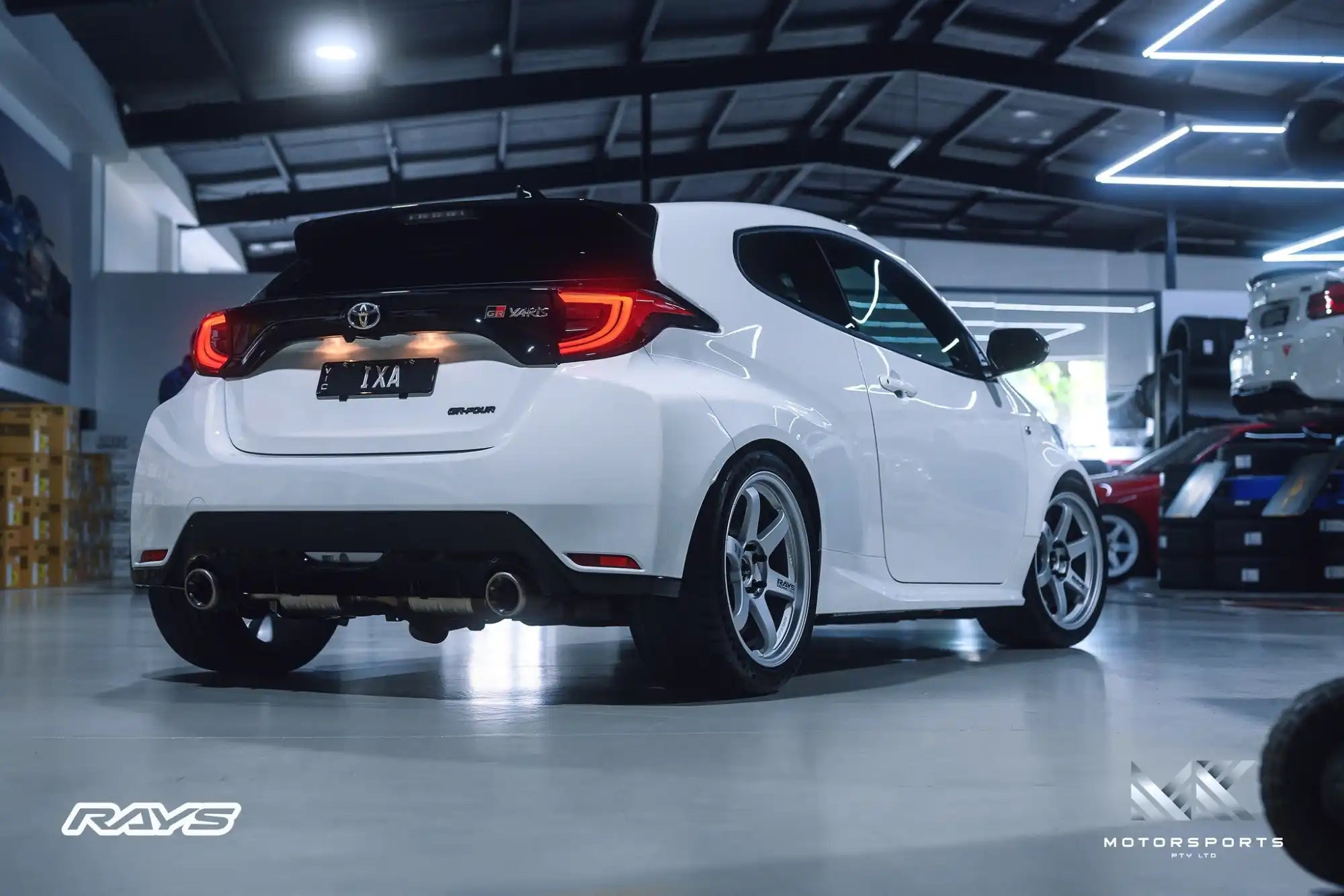 White two-door hatchback with custom wheels and dual exhaust.
